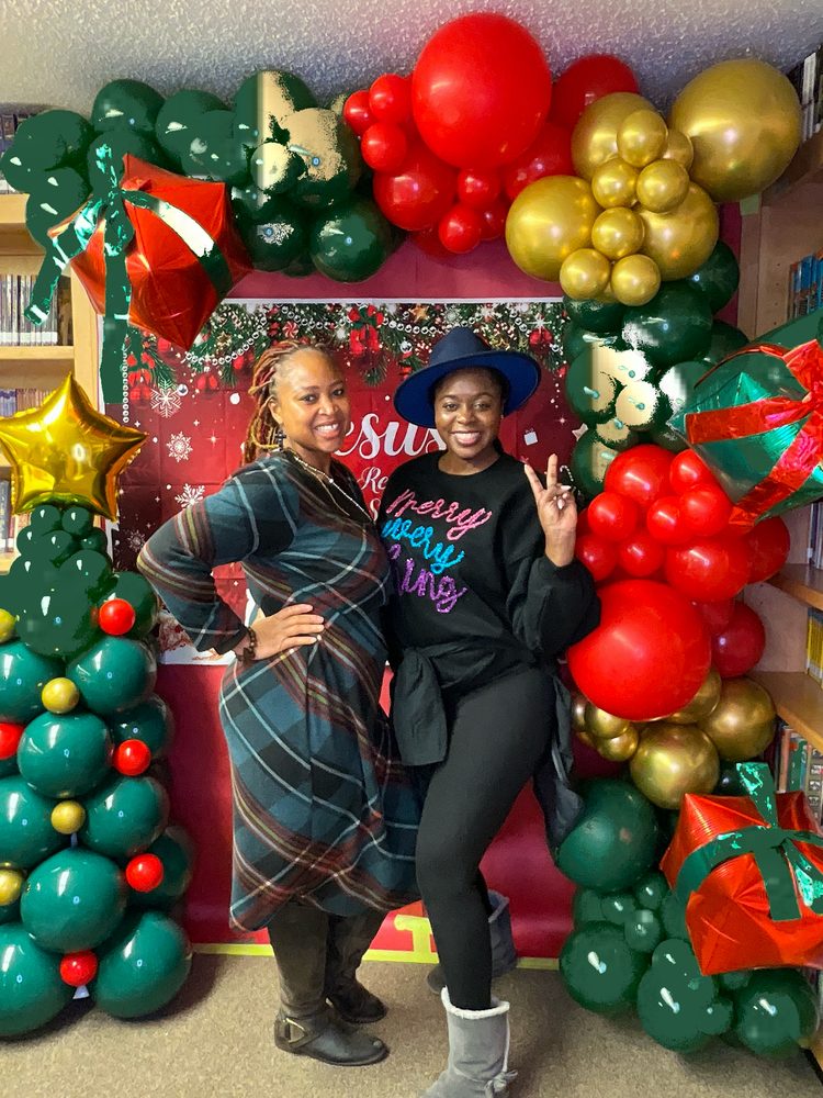 Two friends posing at a festive Christmas balloon garland backdrop