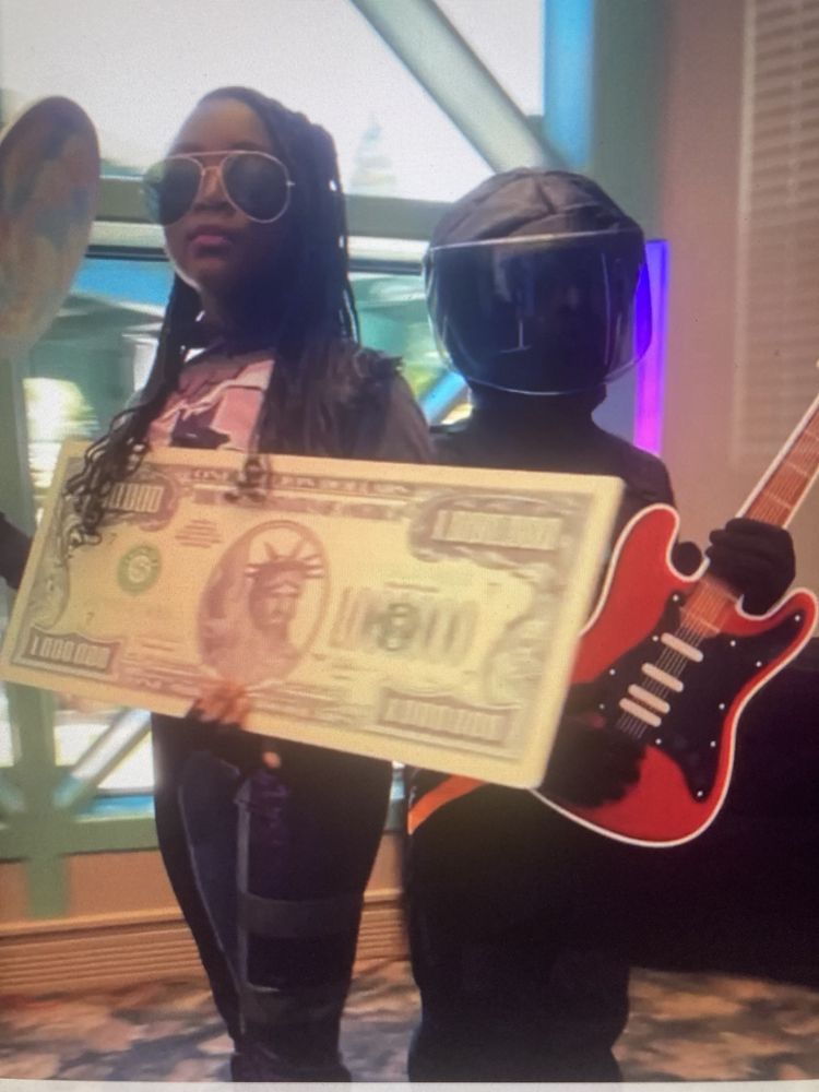 Guests posing with giant money and guitar props at a themed event